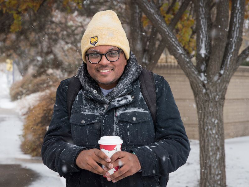 A student stands in the snow holding a hot coffee