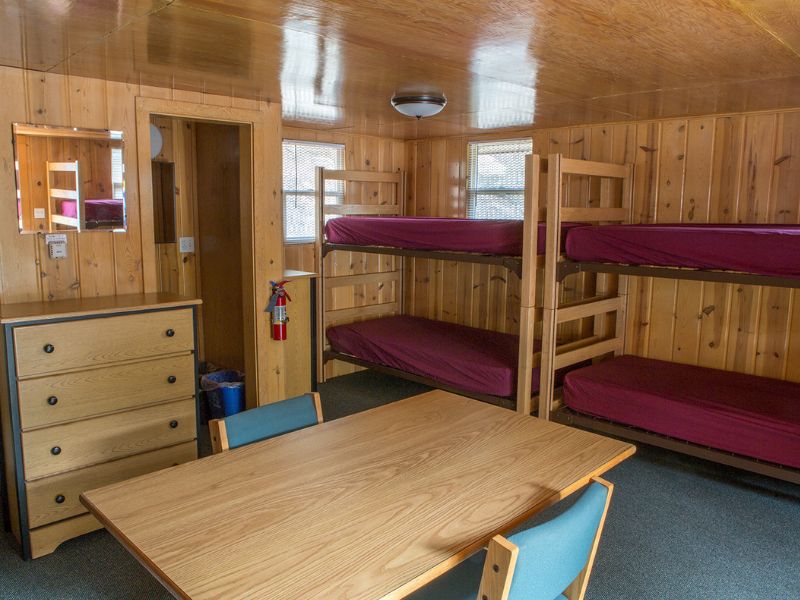 A bunkroom featuring a table, a dresser, and four bunked beds
