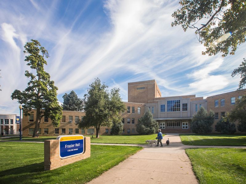 A person walks two dogs near Frasier Hall