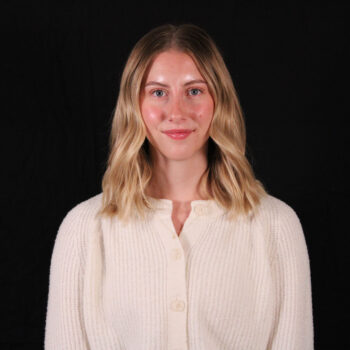 A woman smiling, dressed in a white sweater, against a black background