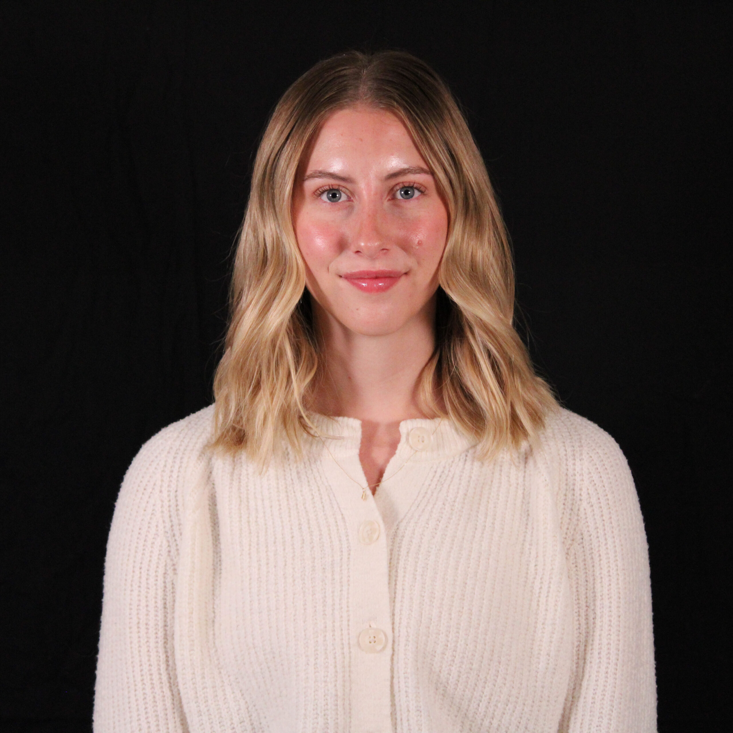 A woman smiling, dressed in a white sweater, against a black background