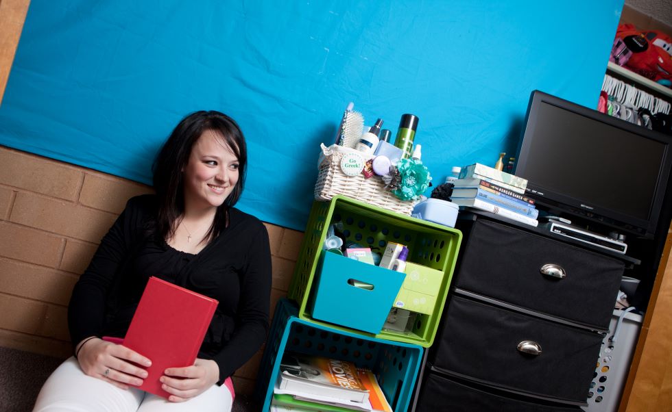 Student smiling sitting next to her bookshelf