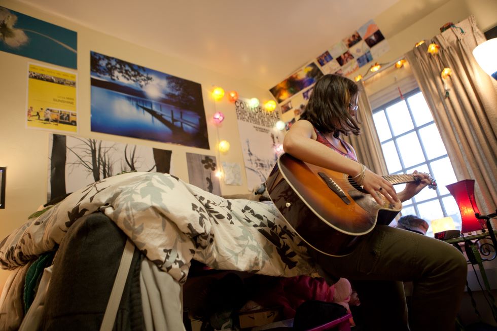 Student strumming guitar in her room
