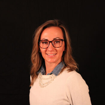 A woman smiling, dressed in a white sweater, against a black background