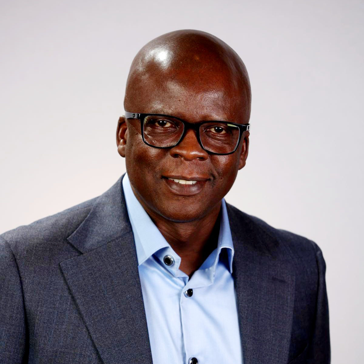 A man with black glasses, dressed in a blue suit. Smiling for a picture.
