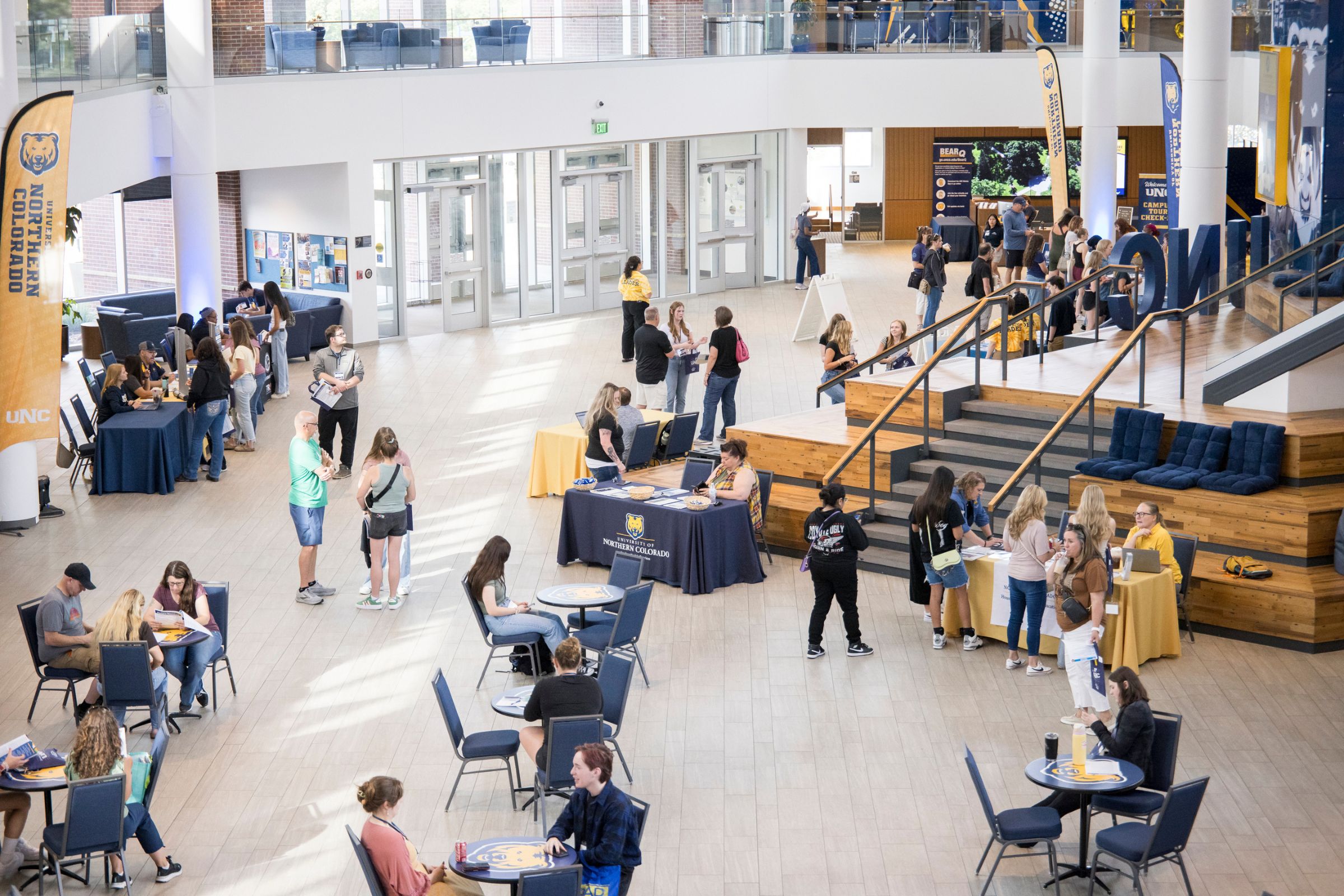 Students and families check in at tables inside a large bright campus atrium decorated with UNC banners and staffed by orientation leaders.