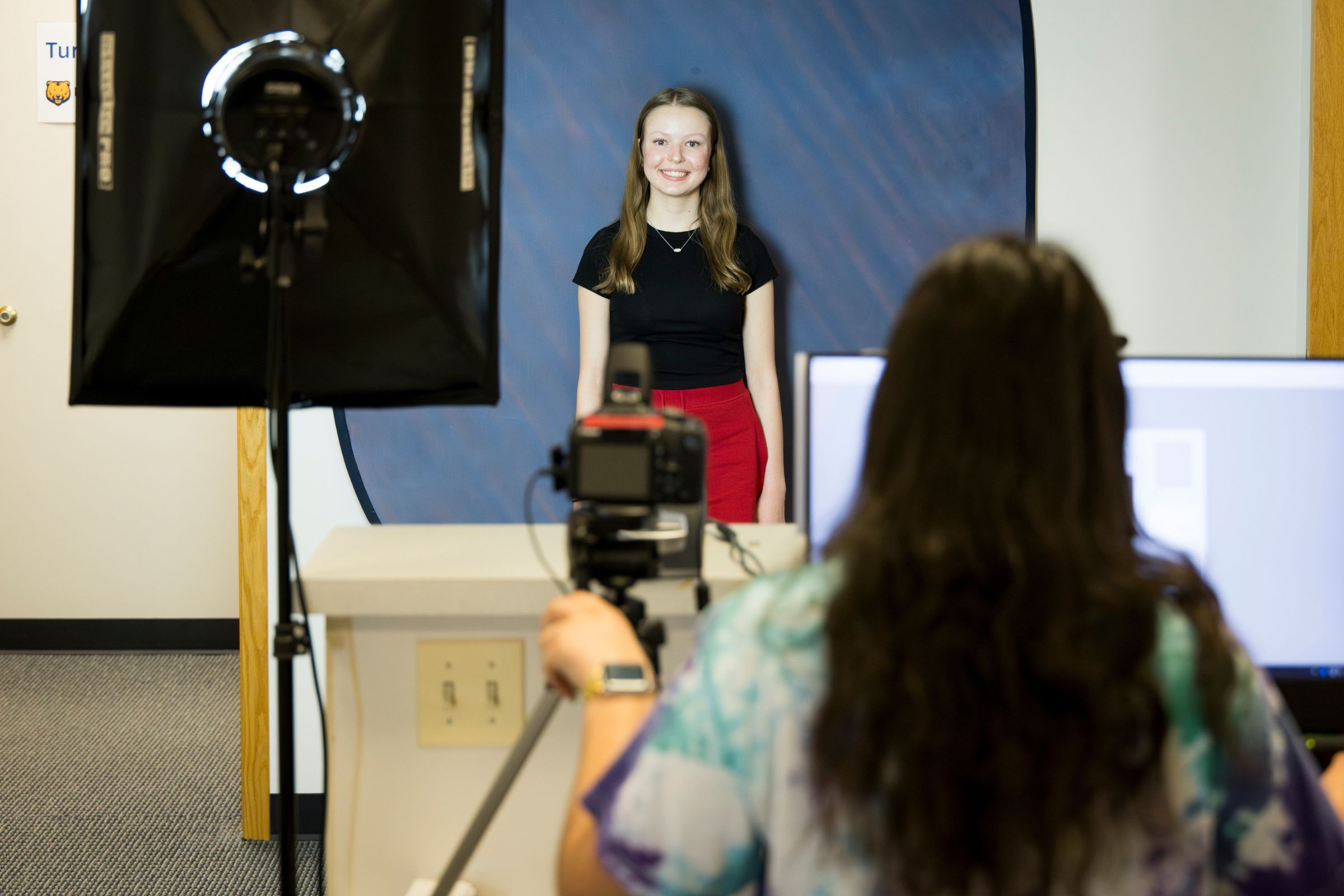 A student poses and smiles for her official UNC ID photo while a photographer captures the image with professional lighting.