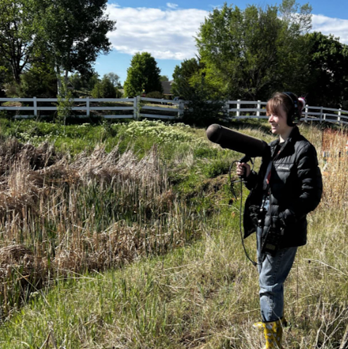Chris Walker conducting summer field research holding a large microphone to record bird song.