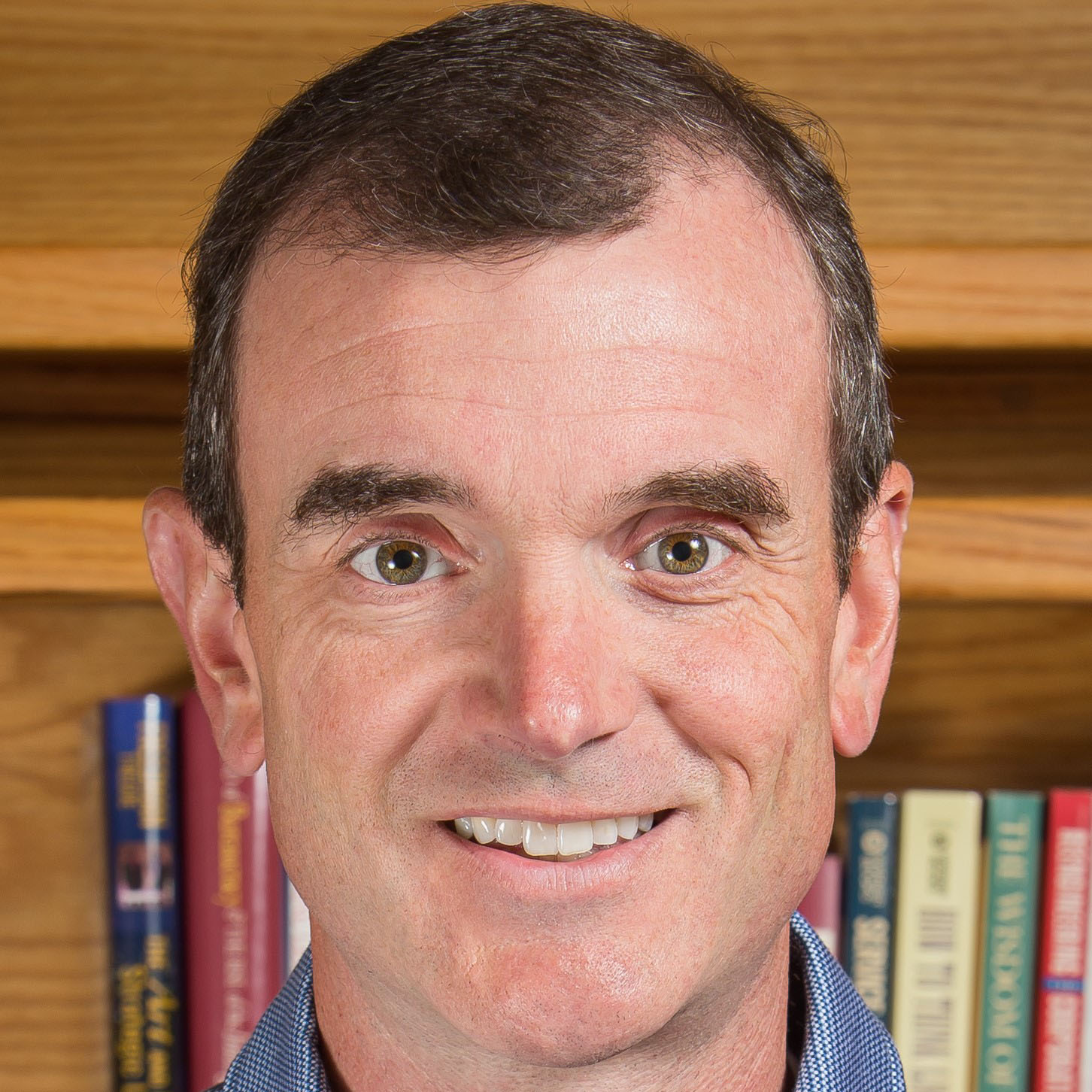 A man smiling, against a background with books.
