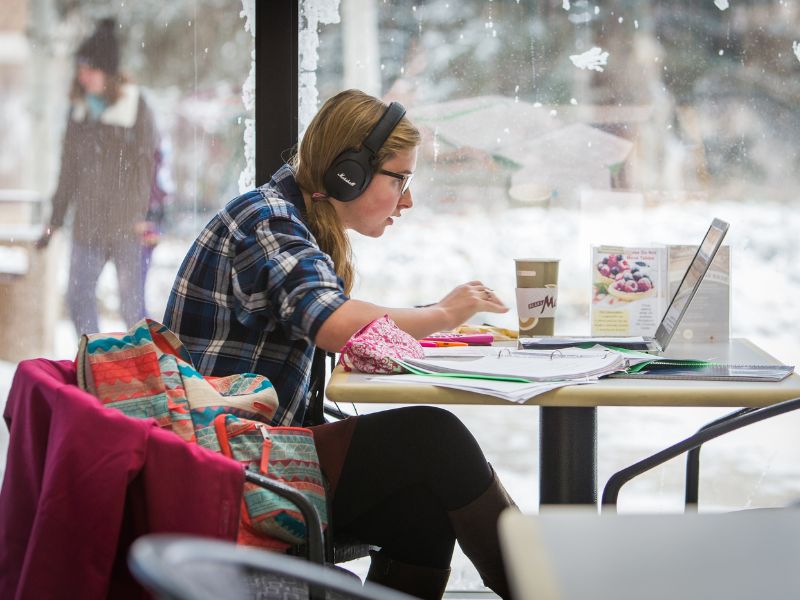 A student drinks coffee and works on their laptop in the University Center
