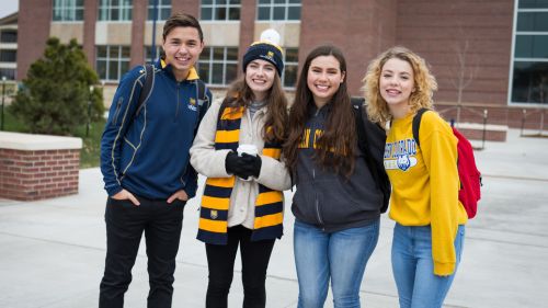 UNC students in blue and gold apparel smiling in front of Campus Commons.