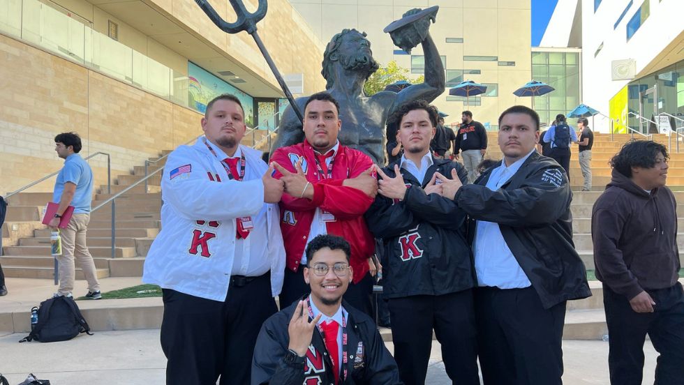 Members of a fraternity pose for a group photo in front of a Poseidon sculpture