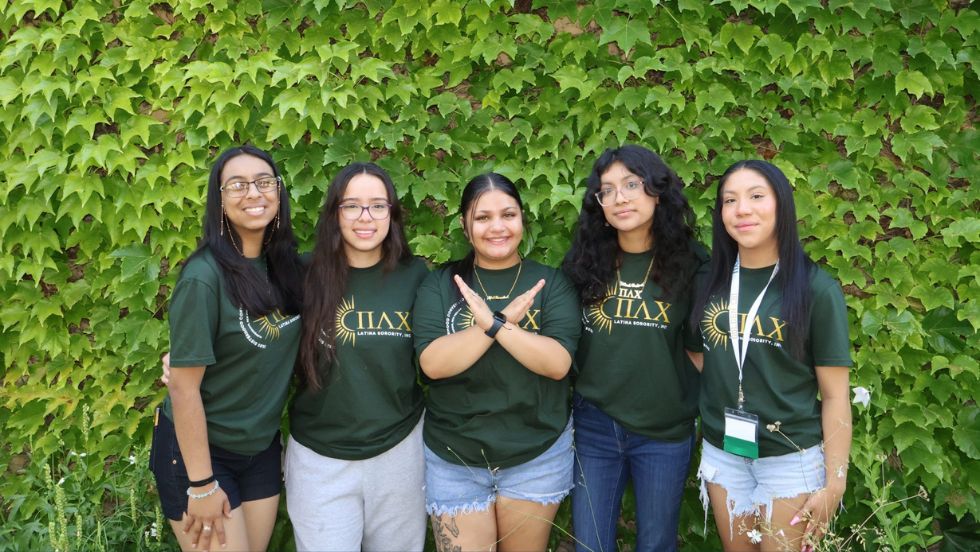 Sorority members pose for a group photo in front of a leafy backdrop