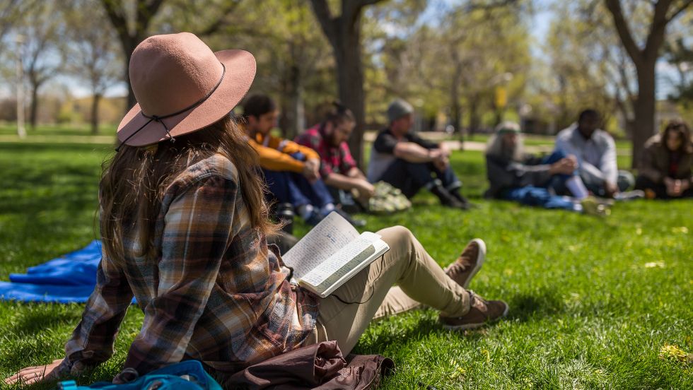 Students reading a book and having a discussion on a campus quad