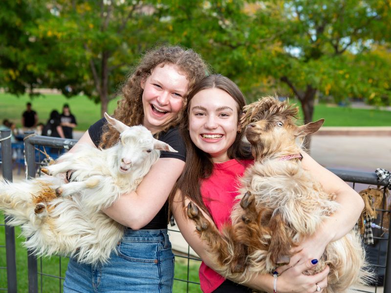 Students pose holding goats at UPC's petting zoo