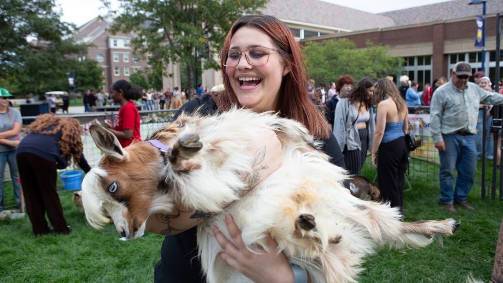 A student poses while holding a goat at a Student Affairs petting zoo
