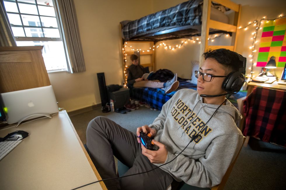 Student using game controller in residence hall room with roommate