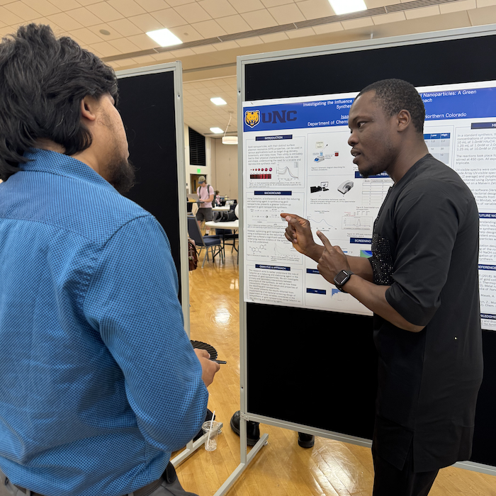 Student presenting poster to an onlooking student at the 2025 Student Showcase of Artists and Scholars