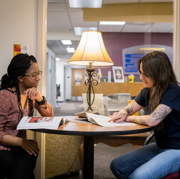 Student Meeting with an Honors advisor in the honors lounge. Lamp in the middle. In the background is the Undergraduate Academic Engagement Sign.