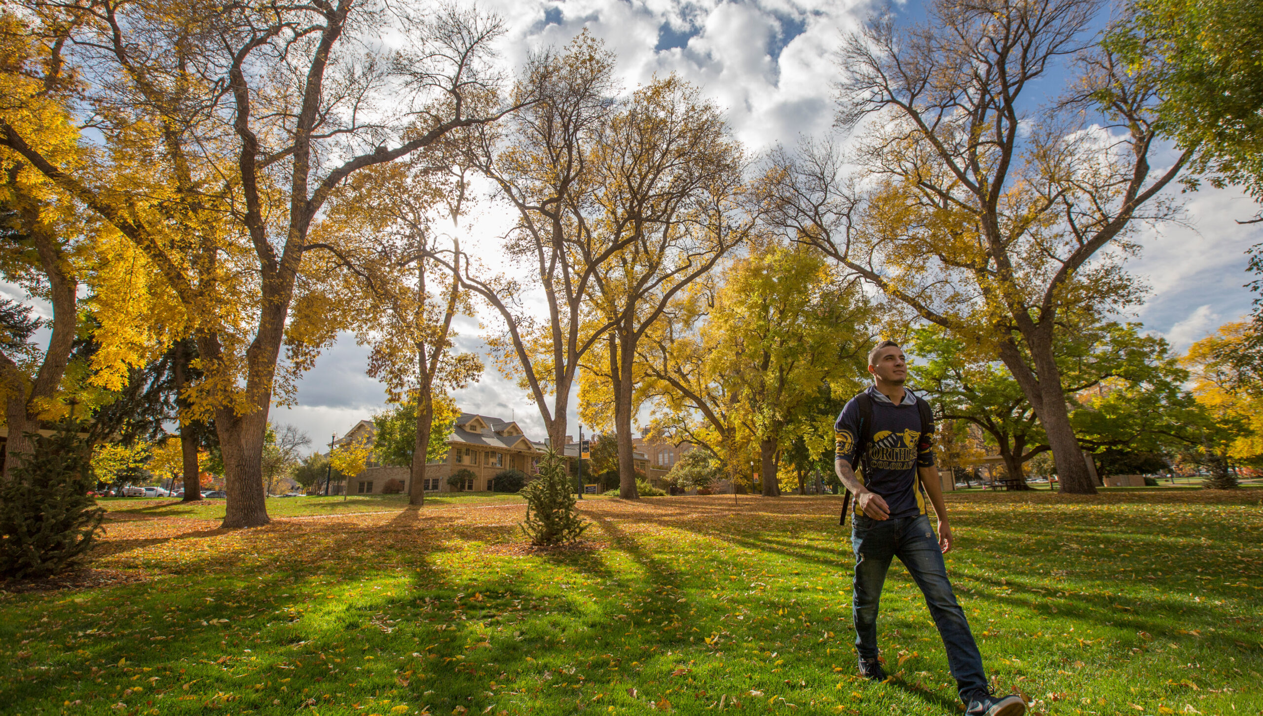 A male student walking, fall leaves in the background