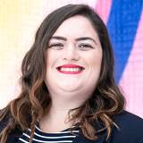A woman smiling with dark hair, with red lipstick on and behind a colorful background. 