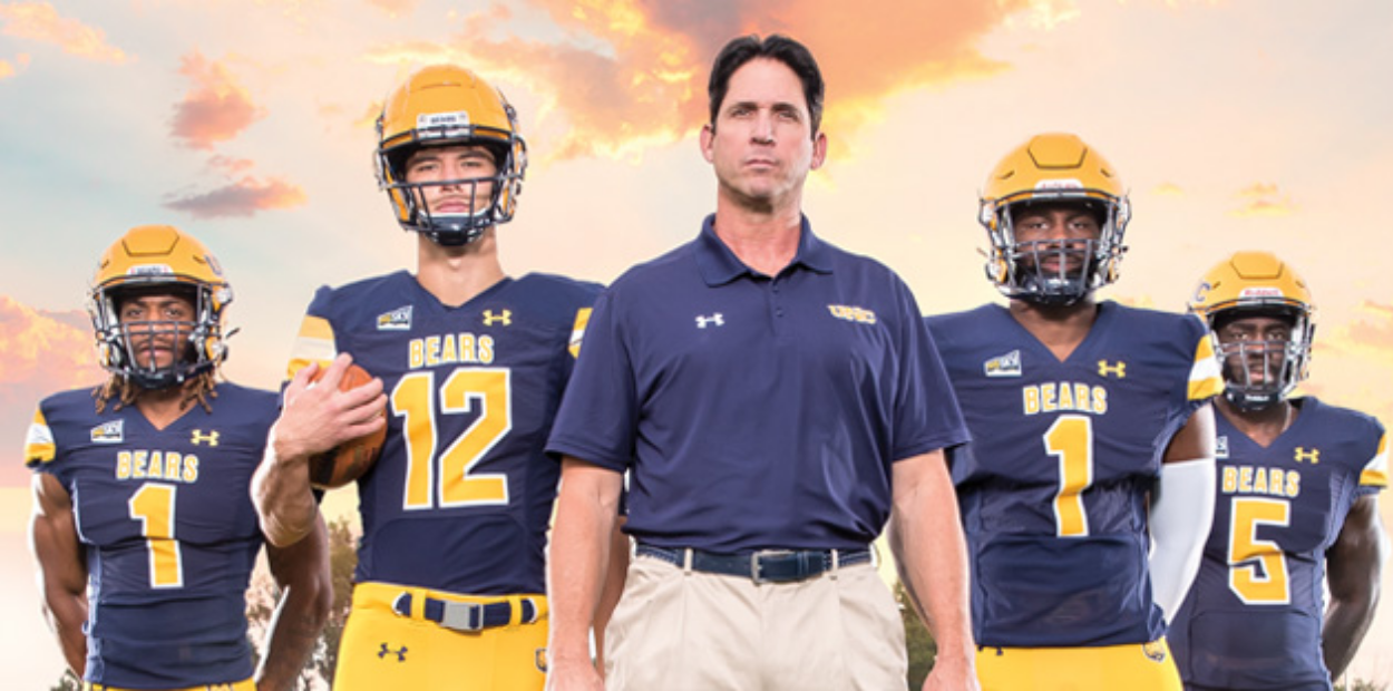 UNC football coach Ed McCaffrey standing in a line next to four UNC football players.