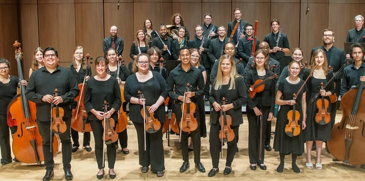Orchestra musicians posing together holding their instruments and smiling