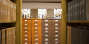 This picture shows the inside of the library, with shelves of books in the foreground and a card catalog in the background.