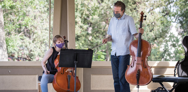 Two people playing the cello wearing face masks