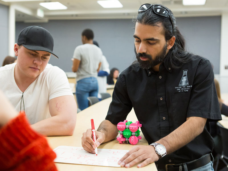 Graduate assistant drawing out a chemistry formula while a student looks on.