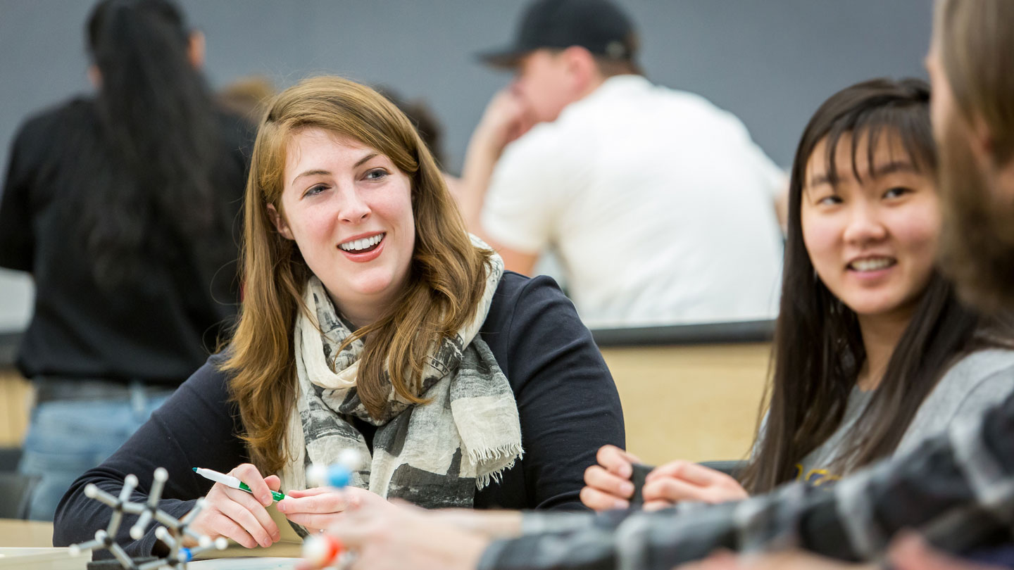 Student, on left, looking at another student, on the right, with a third student in-between.