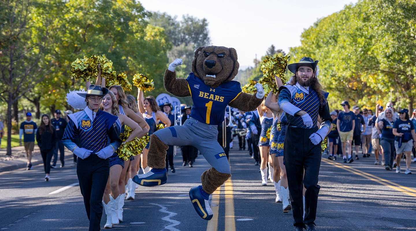 Homecoming pep rally with UNC band, cheerleaders, and Klawz the UNC mascot jumping.