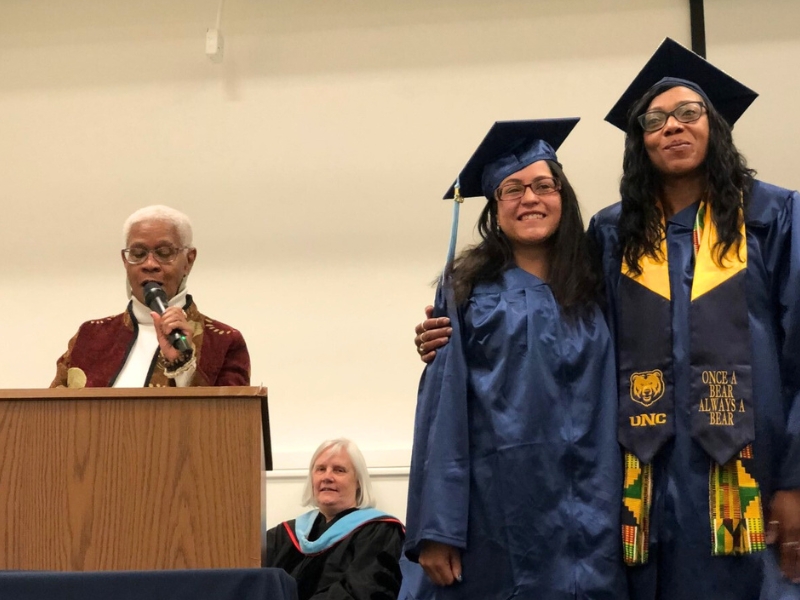 Two students standing at graduation in their cap and gown on stage