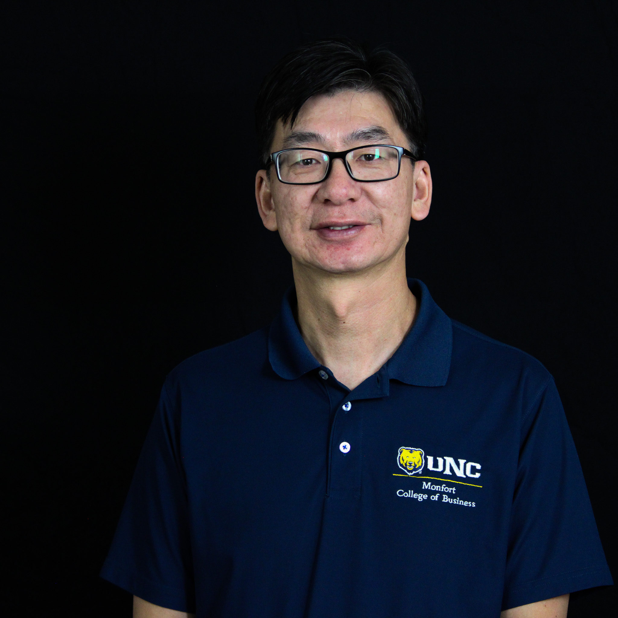 A man dressed in a UNC polo, smiling, against a black background