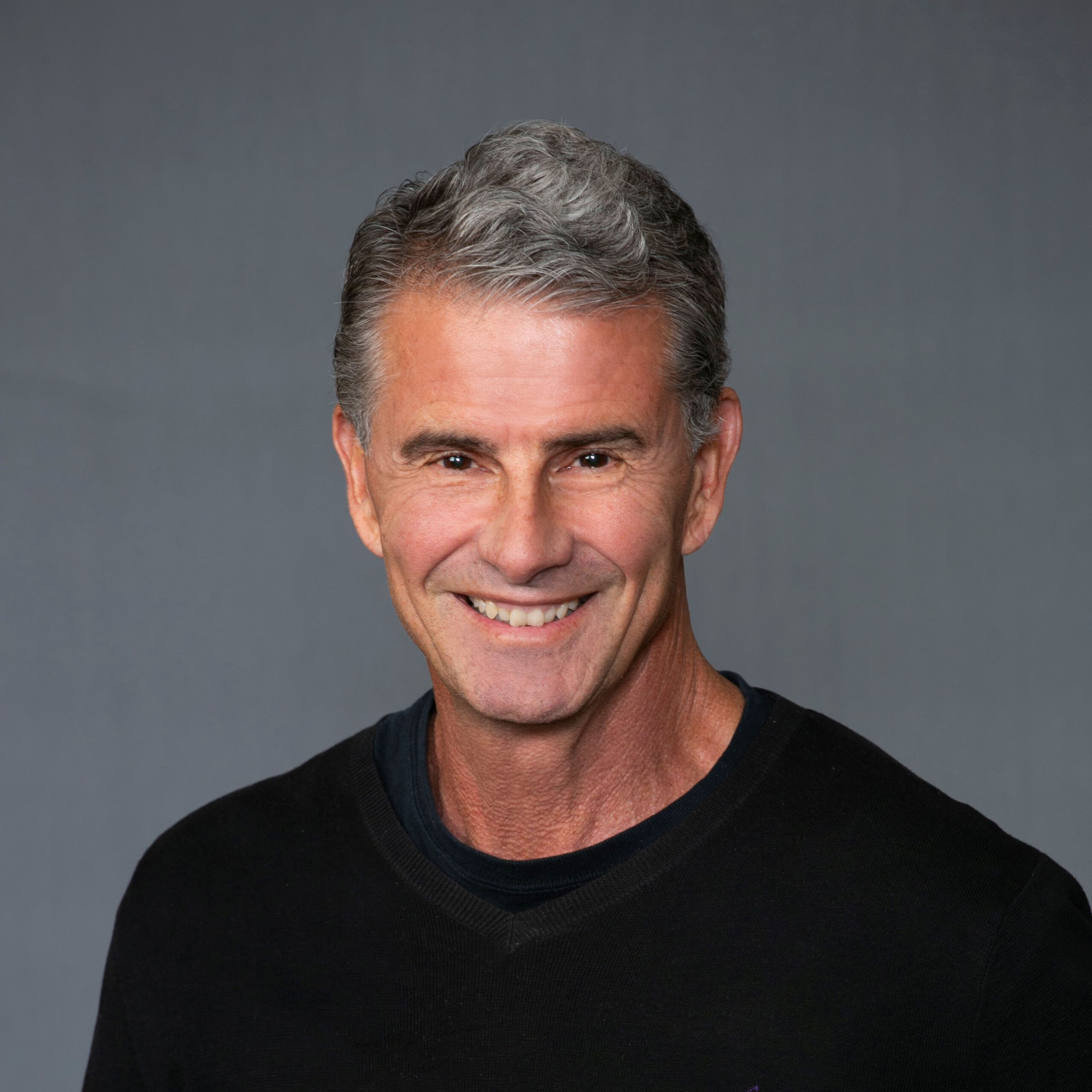 A man with gray hair, dressed in a black shirt, smiling for a picture