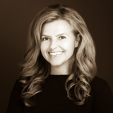 A woman smiling, with long hair, against a black background. 