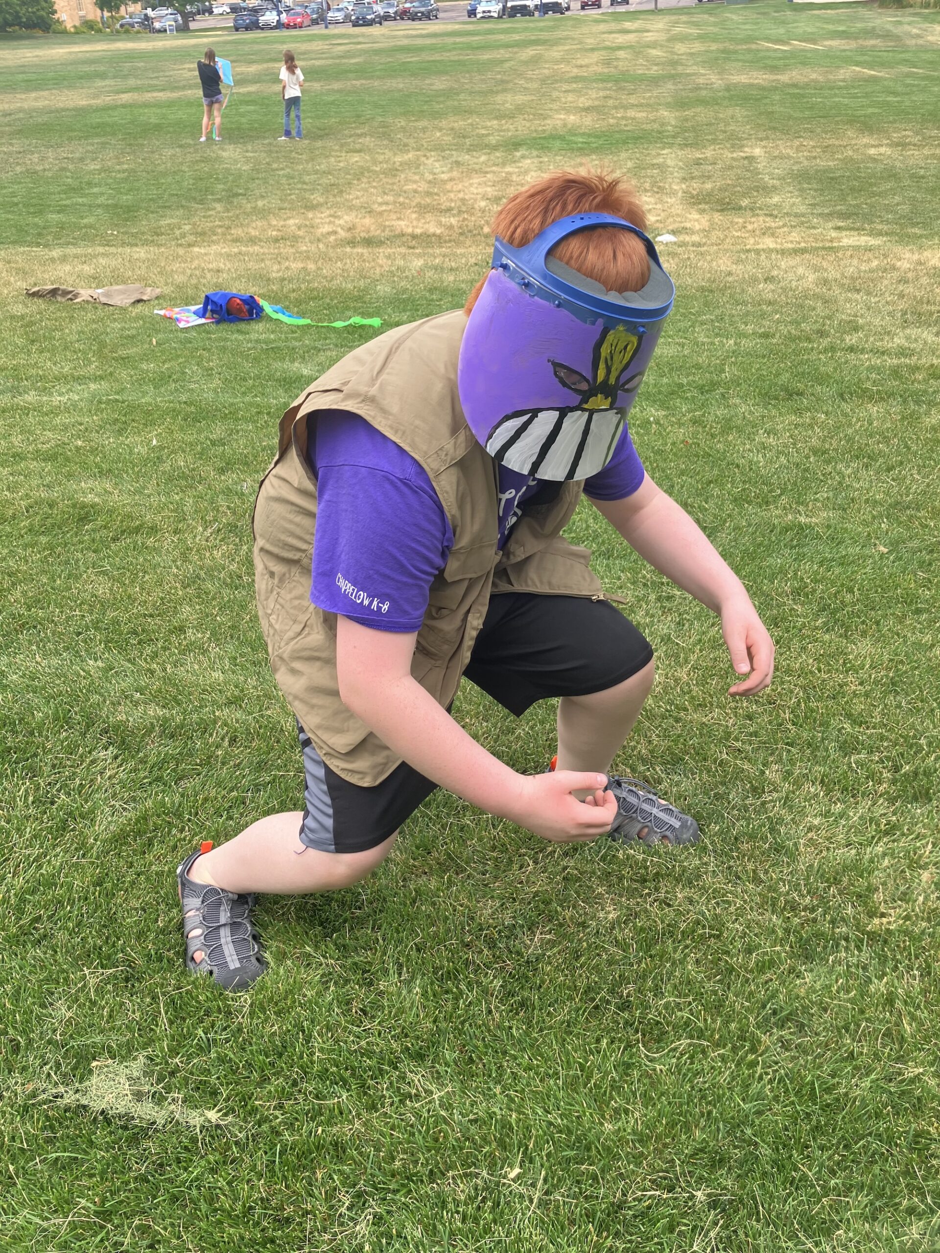 Student wearing the mask he made and crouching down at Exploring Arts Camp.