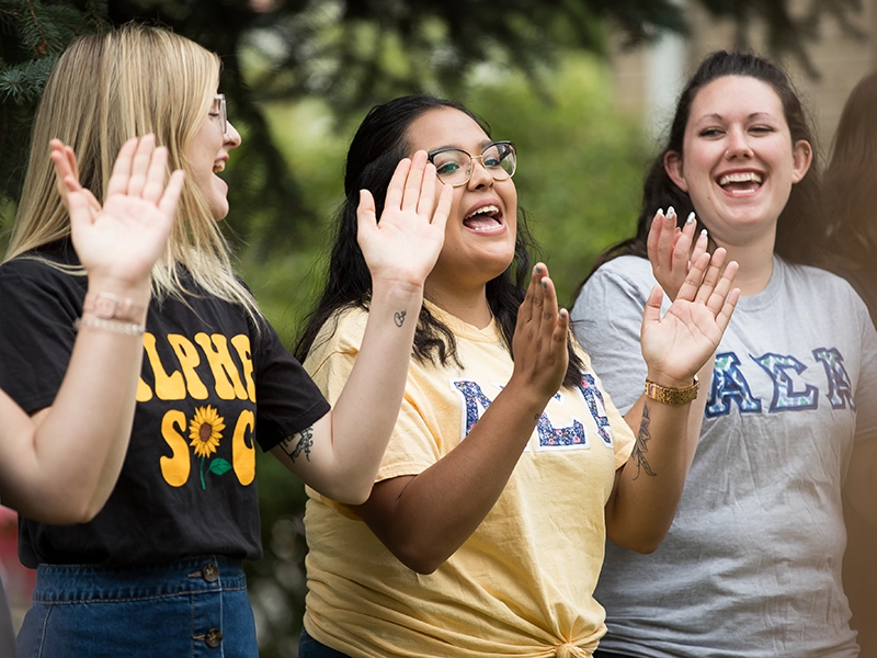 Three female students clap and smile, celebrating their sorority experience together.