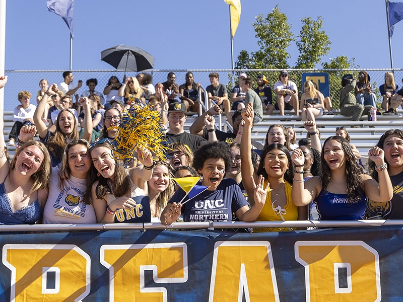 UNC students cheering together at a football game, celebrating with school spirit and chanting “Go Bears!”
