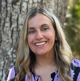 A woman smiling, blonde hair, with a tree in the background. 