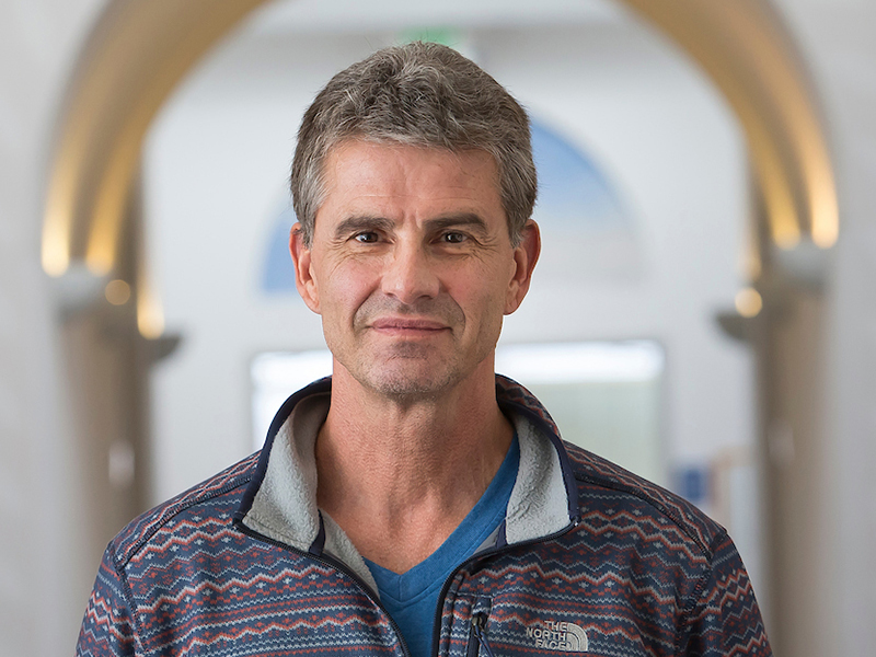 a man with a colorful zip up hoodie, grey hair, smiling profile picture
