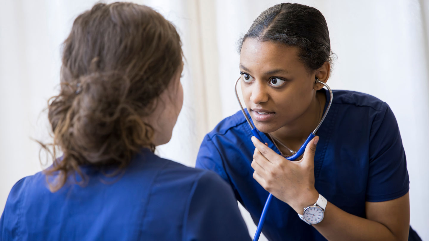 Nursing student with stethoscope listening to the heartbeat of another person.