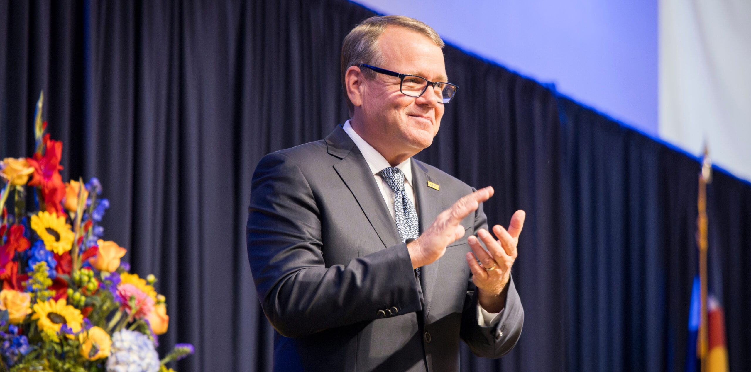 President Andy Feinstein clapping while giving a speech on a stage