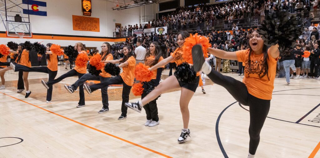 Cheerleaders wearing black and orange kicking their leg up