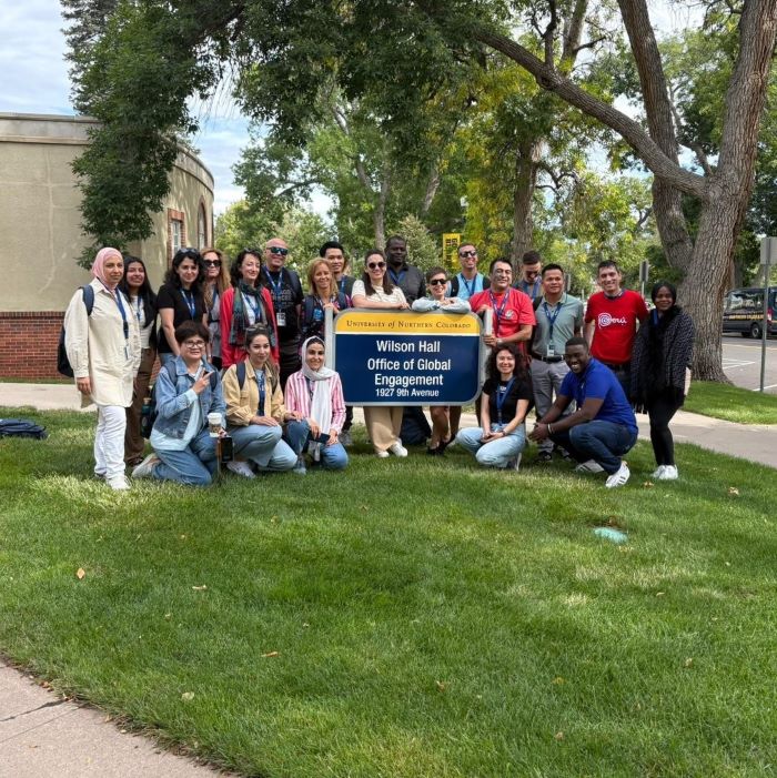 Group of visiting scholars standing in front of the Office of Global Engagement sign on the Wilson Hall lawn