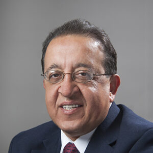A man with glasses, smiling, dressed a nice blue suit with a red tie.