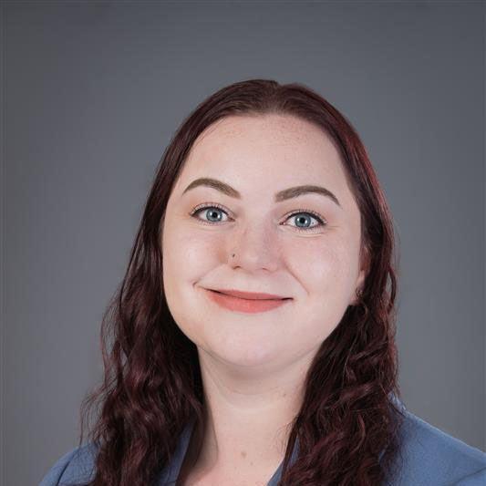 A woman with red hair, smiling, against a dark grey background