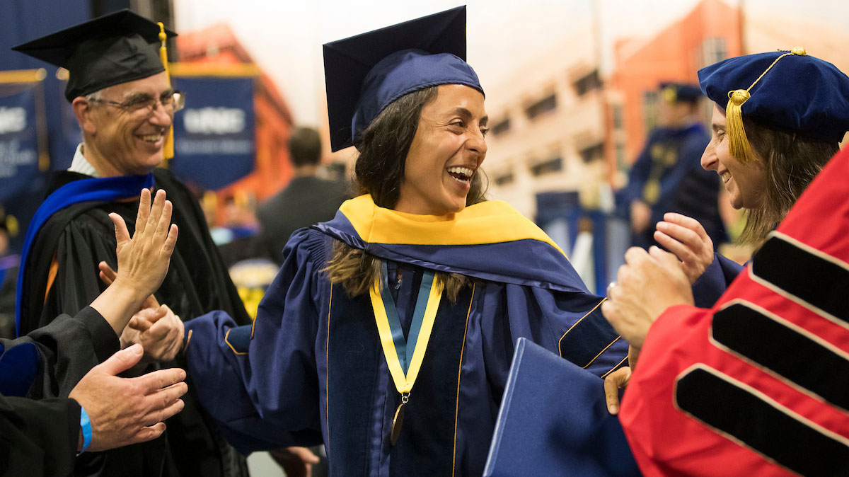 A woman wearing a graduation gown and cap smiling, surrounded by other people smiling