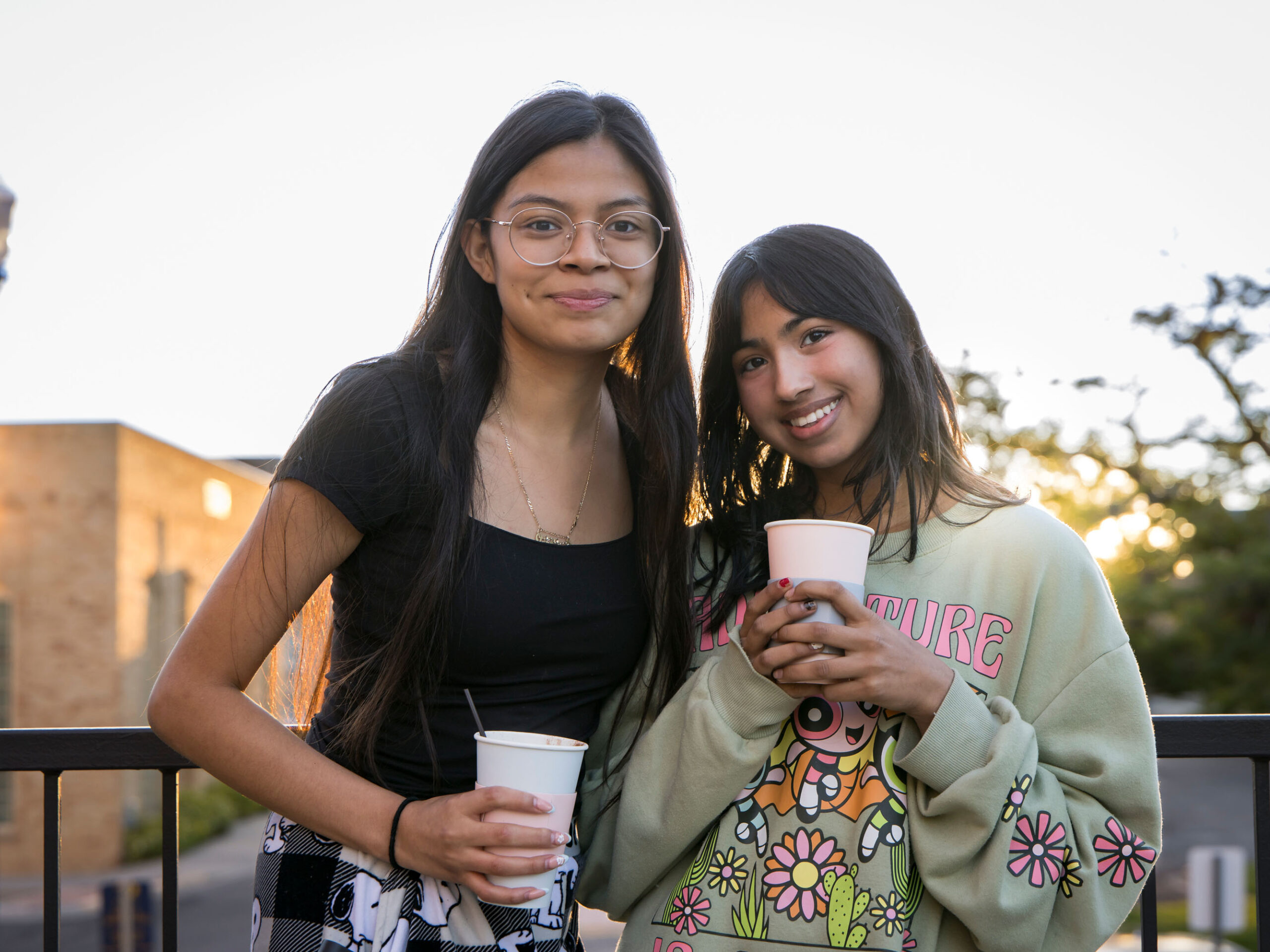 Two friends enjoying drinks outdoors, smiling and relaxed in casual attire.