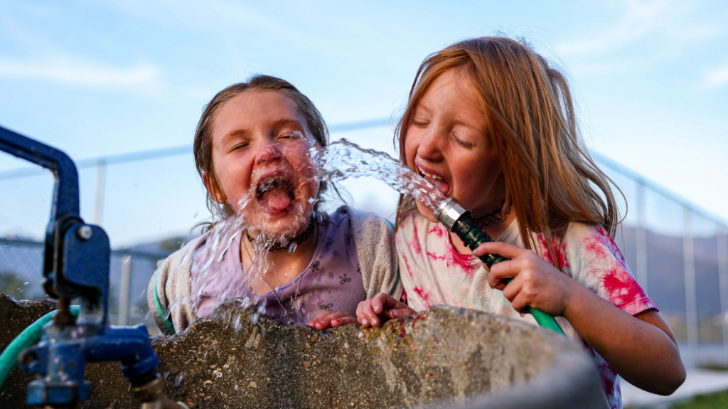 Two kids drinking water out of the hose